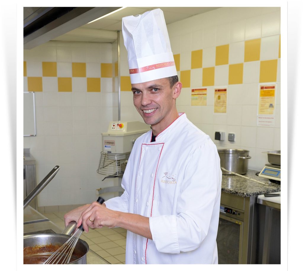 Chef gérant souriant en cuisine en restauration collective.