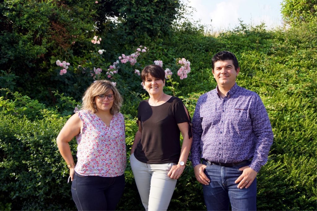 Trois membres de l'équipe du Savoir Partagé devant un buisson.